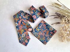 four pieces of blue and pink floral patterned tie next to dried flowers on a white surface