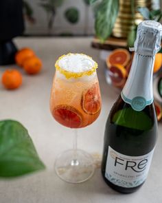 a bottle of wine next to a glass filled with ice and oranges on a table