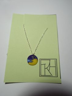 a necklace with a blue and yellow disc hanging from it's center on a card