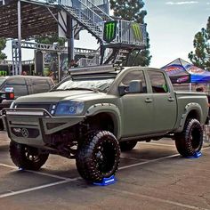 a green truck parked in a parking lot next to other trucks and people standing around