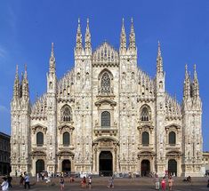 people are walking around in front of a large building with many spires on it