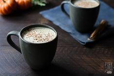 two mugs of coffee sitting on top of a wooden table next to pumpkins