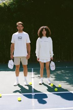 two people standing on a tennis court holding racquets and balls in their hands