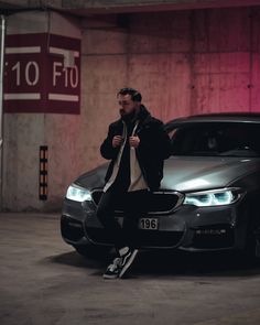 a man sitting on the hood of a car in a parking garage next to another car