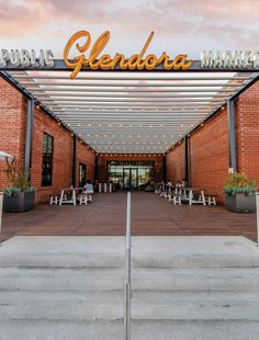 the front entrance to a public market with tables and benches under a sign that reads,