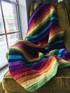 a multicolored crocheted blanket sitting on top of a chair next to a window