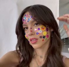 a woman with colorful face paint posing for the camera and holding her hand up in front of her face