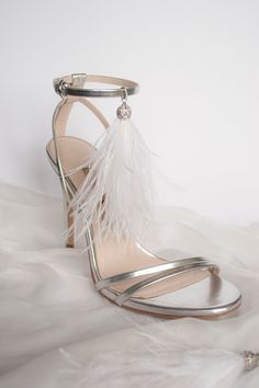 a pair of silver high heeled shoes with feathers on the toes and ankle straps