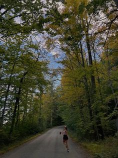 a woman running down the middle of a road in front of some trees and bushes