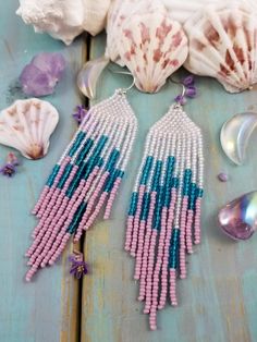 pink and blue beaded earrings with seashells on the table next to them