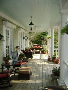 a porch with rocking chairs and potted plants on the back deck, surrounded by white pillars