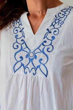 a woman wearing a white shirt with blue embroidery on it