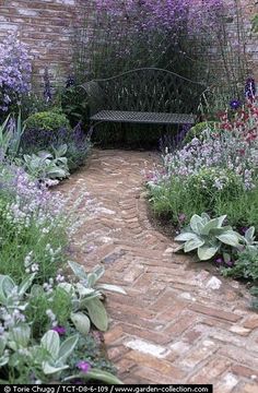 a brick path leads to a bench in the middle of a garden filled with flowers