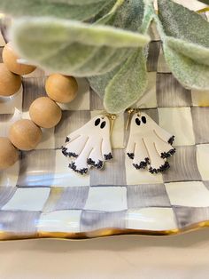 two white ghost earrings sitting on top of a checkered plate