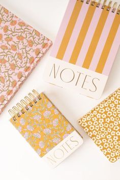 three notebooks sitting next to each other on top of a white table with flowers