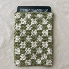 a green and white crocheted ipad case sitting on top of a bed next to a tablet