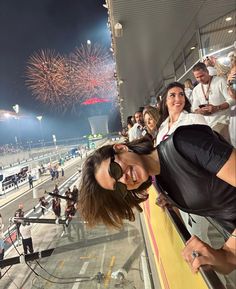 a woman leaning against a wall with fireworks in the sky above her and people watching