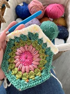 a person holding a crochet pot holder in front of some balls of yarn