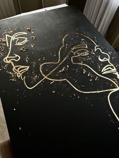 a black table with gold paint on it and a drawing of a woman's face