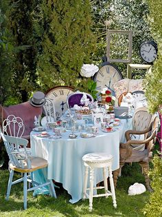 there is a table set up with tea cups and saucers on it in the grass