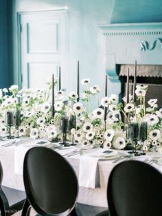 the table is set with white flowers in vases and silver candlesticks, along with black chairs