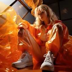 a woman sitting on the ground with her legs crossed and wearing white sneakers, an orange shirt and pants