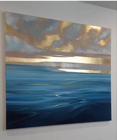 a painting hanging on the wall with blue water and gold clouds in the sky above it