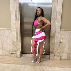 a woman standing in front of an elevator wearing a pink and white skirt with high heels