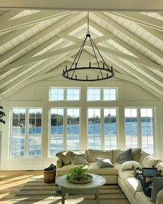 a living room filled with white furniture and windows next to a large body of water