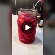 a glass jar filled with liquid sitting on top of a white table next to a spoon