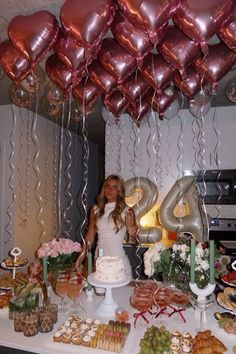 a woman standing in front of a table full of food and balloons with the number 20 on it