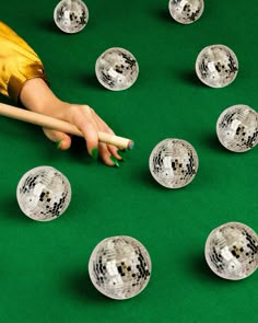 a woman's hand reaching for some disco balls on a green table with white sticks