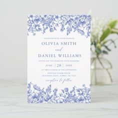 a blue and white wedding card with flowers on the front, in front of a vase