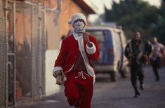 a man dressed as santa claus running down the street with other people walking behind him