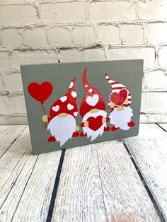 two gnomes with heart balloons are painted on a wood block in front of a brick wall