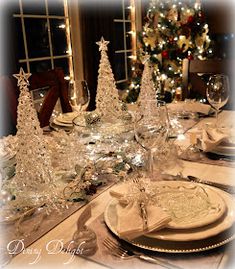 a dining room table set for christmas with white plates and silverware, trees in the background