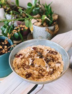 a bowl of oatmeal sitting on top of a table next to potted plants