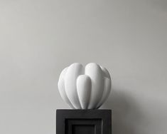 a white vase sitting on top of a black square frame in front of a gray wall