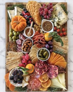 an assortment of cheeses, meats and fruits on a platter with crackers