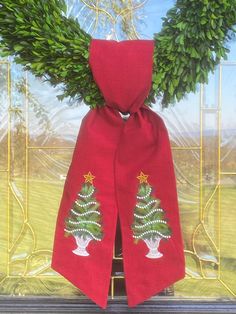 a red scarf with a christmas tree on it and two green wreaths behind it