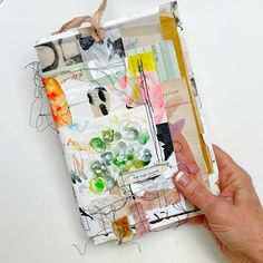 a person is holding a piece of art made out of scrap paper and other items