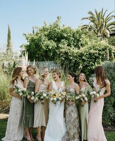 a group of women standing next to each other in front of trees and bushes holding bouquets