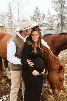 a pregnant woman standing next to a brown horse while her husband kisses her belly in front of them