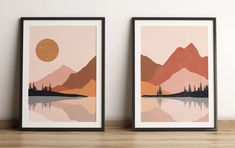 two framed art prints on a shelf next to each other with mountains in the background