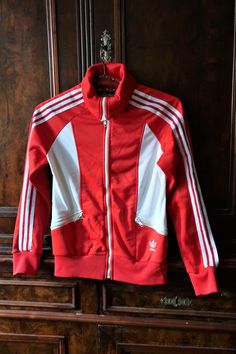 Beautiful Vintage Adidas track jacket from the 1980s. Slightly shiny red fabric with white inserts on the sides and on the back. Raglan sleeves, YKK front zipper, two zipped front pockets. Embroidered Adidas Trefoil on the left waist. Elasticated cuffs and waistband. Iconic stripes along the sleeves. Fleeced inside. Made in France! Amazing 80s Vintage piece - combine casual with sneakers, jeans or track pants! ERA: 1980s BRAND: Adidas COLOR: Red, white FABRIC: 54% polyester, 46% triacetate SIZE: Luxury Track Jacket For Sports, Red Sporty Track Jacket With Three Stripes, Sporty Red Outerwear With Three Stripes, Retro White Track Jacket For Sports, Red Track Jacket With Three Stripes, Red 90s Style Track Jacket For Fall, 90s Red Fall Track Jacket, 90s Style Red Track Jacket For Fall, 90s Red Track Jacket For Sports