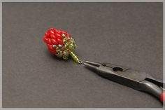 a pair of pliers with red beads on it and a green beaded flower