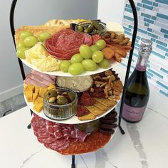 a three tiered platter filled with meats, cheeses and olives next to a bottle of wine