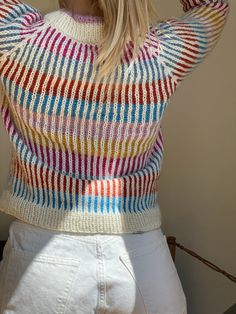 a woman with blonde hair wearing a multicolored sweater and white shorts is looking off to the side