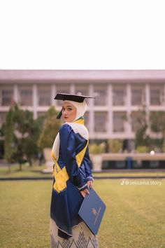 a woman wearing a graduation gown and holding a book is standing in front of a building