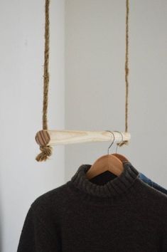 a sweater hanging from a wooden hanger on a white wall next to a black shirt